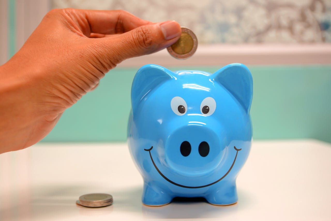our-story Hand inserting a coin into a blue piggy bank for savings and money management.