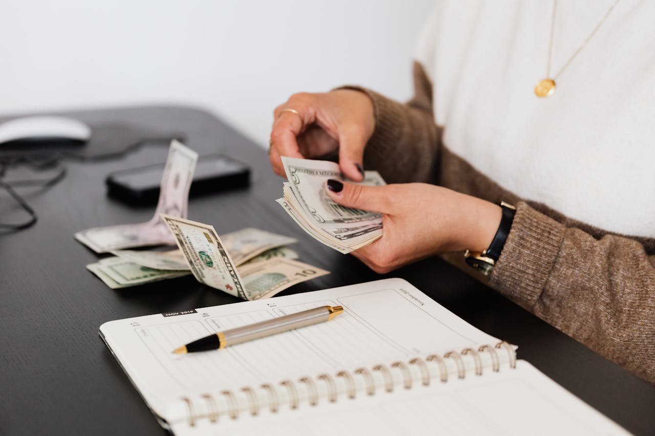 about-us Close-up of person counting cash with notepad on desk, indicating financial tasks.